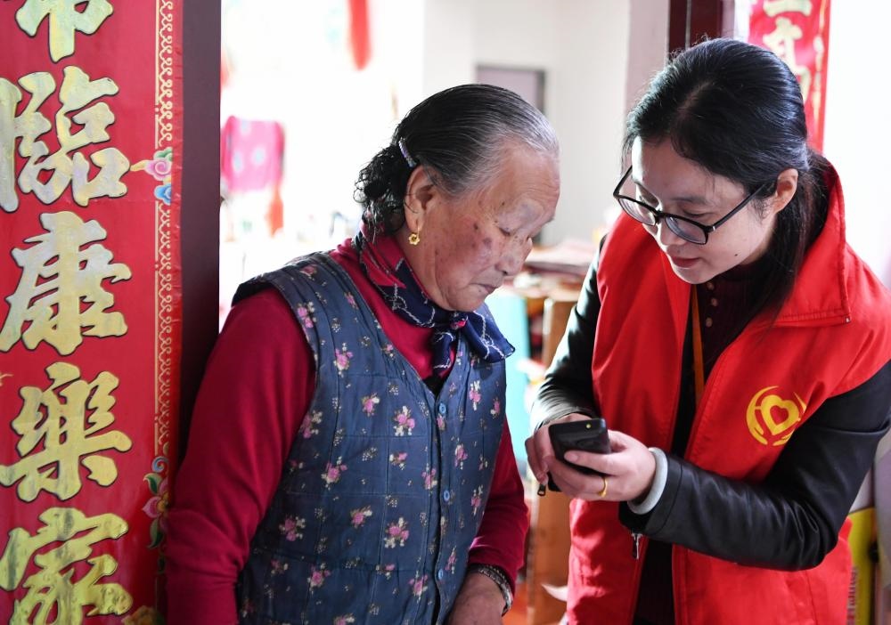 在福州市長樂區(qū)航城街道籌岐村，智慧養(yǎng)老平臺派駐社區(qū)的助老員（右）在為老人陳鳳英（左）講解養(yǎng)老定制手機(jī)的用法（2021年11月26日攝）。新華社記者 魏培全 攝