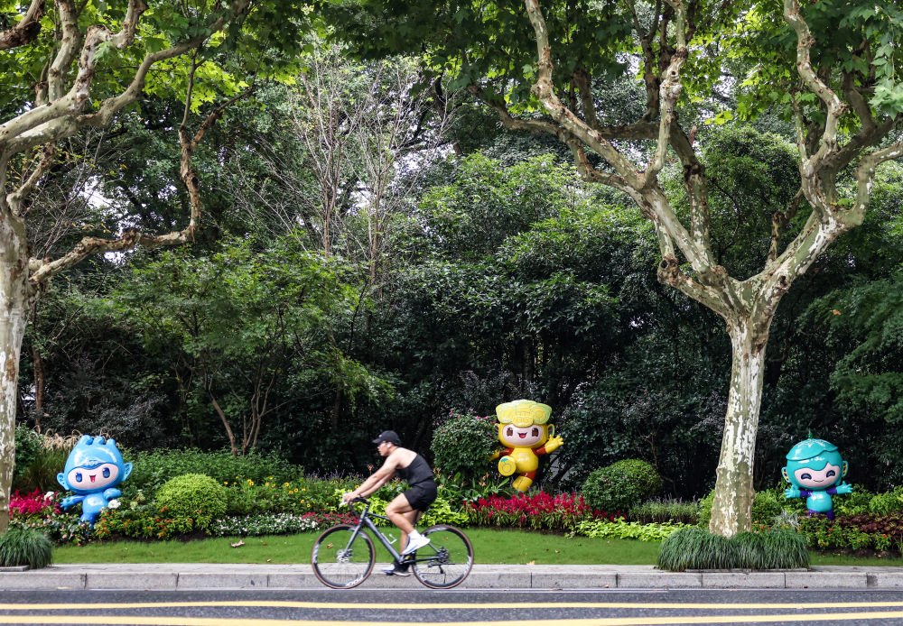 市民在杭州市南山路上一處亞運會主題吉祥物雕塑前騎自行車。